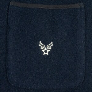 May include: A dark blue fabric pocket with a white embroidered emblem of a star with wings.