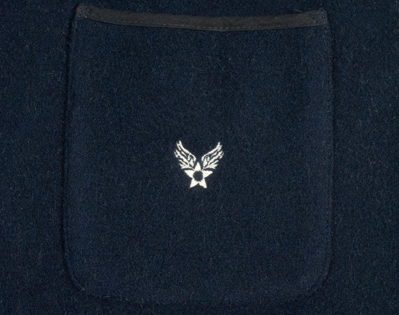 May include: A dark blue fabric pocket with a white embroidered emblem of a star with wings.