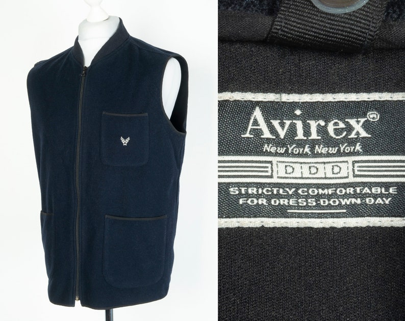 May include: A navy blue fleece vest with a zipper closure and two front pockets. The vest has a small embroidered logo on the left chest pocket. The label on the vest reads "Avirx New York New York DDD Strictly Comfortable For Dress-Down-Day"
