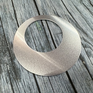 Puede incluir: Un anillo de metal plateado con un acabado liso cepillado y una abertura circular en el centro.