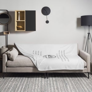Può includere: Coperta in pile bianco con testo nero che recita: "L'unico modo per elevarsi è praticare l'auto-credo di fronte al dubbio."