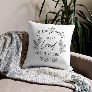Könnte beinhalten: Ein weißes Kissen mit schwarzem Text, der "Give thanks to the Lord for he is good, Psalm 107:1" lautet. Der Text ist von zwei schwarzen Blattmotiven umgeben.