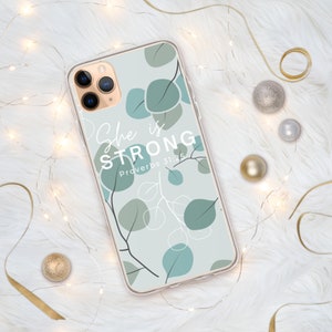May include: A clear phone case with a light blue background and a white floral design. The text "She is STRONG Proverbs 31:25" is printed on the case.