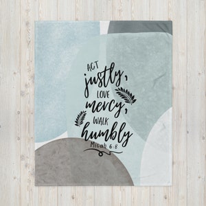 May include: A soft, blue and gray throw blanket with a white background. The blanket features a quote in black lettering: "Act justly, love mercy, walk humbly Micah 6:8".