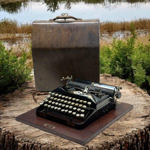 Puede incluir: Una máquina de escribir vintage negra con una caja de transporte de madera marrón. La máquina de escribir tiene un cuerpo de metal y un teclado con teclas redondas. La caja tiene un asa y un cierre.