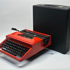 May include: A red vintage Olivetti Lettera 32 typewriter with a black carrying case. The typewriter has a black keyboard and a black carriage return lever.