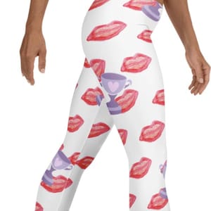 Peut inclure: Legging blanc avec un motif répété de lèvres rouges et de motifs de coupes de trophées violets. Le legging est moulant et fabriqué dans une matière extensible, adapté aux activités sportives ou aux tenues décontractées.