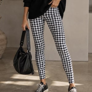 May include: A black V-neck long-sleeve sweater paired with black and white houndstooth print leggings, black leather handbag with a tassel, and black and white low-top sneakers. The outfit features a classic monochromatic color palette.