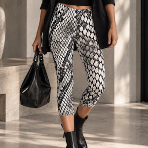Op de afbeelding: Een zwarte blazer, een zwart topje met een ronde hals en een driekwart legging met een zwart-wit slangenprint. De outfit wordt gecombineerd met zwarte enkellaarsjes en een zwarte handtas. Het geheel bevat een donkere zonnebril en een gouden ketting.
