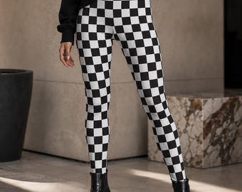 Puede incluir: Un suéter negro de manga larga con cuello de cremallera plateada, combinado con leggings de talle alto con un patrón de cuadros blanco y negro y botines negros con suela gruesa de plataforma.