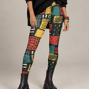 May include: A black chunky knit turtleneck sweater paired with leggings featuring a multicolored abstract patchwork print in shades of yellow, red, and dark green, finished with black leather ankle boots and thick circular bangles.