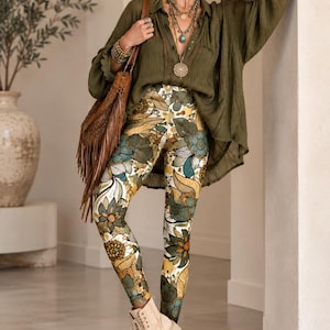 May include: An olive green long-sleeved button-down shirt with a textured finish paired with leggings featuring a multi-colored floral and leaf pattern in shades of mustard yellow, teal, and white, worn with beige lace-up ankle boots and a brown fringe bag.