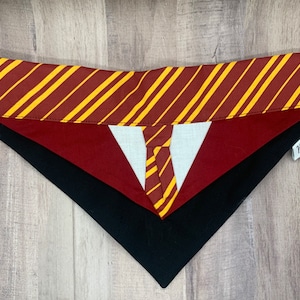 Peut inclure: Un bandana pour chien rouge, noir et blanc avec un motif rayé jaune et rouge. Le bandana a une étiquette blanche avec le mot "Barkin'" dessus.