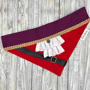 May include: A red and purple dog bandana with a white ruffled collar, black belt, and gold trim. The bandana has a small tag that says "Barkin".