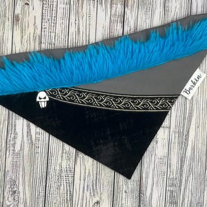 May include: A triangular pet bandana with a black and gray design, trimmed with bright blue faux fur. The bandana features a white graphic and a decorative silver border. The tag reads "Barkin".