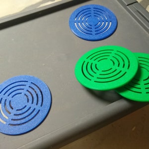 May include: Several round, blue and green objects with a concentric circle design. The objects are arranged on a gray surface. The objects appear to be made of a textured material.