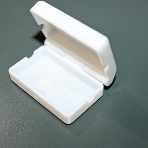 May include: A small, white plastic box with a hinged lid. The box is open and empty.