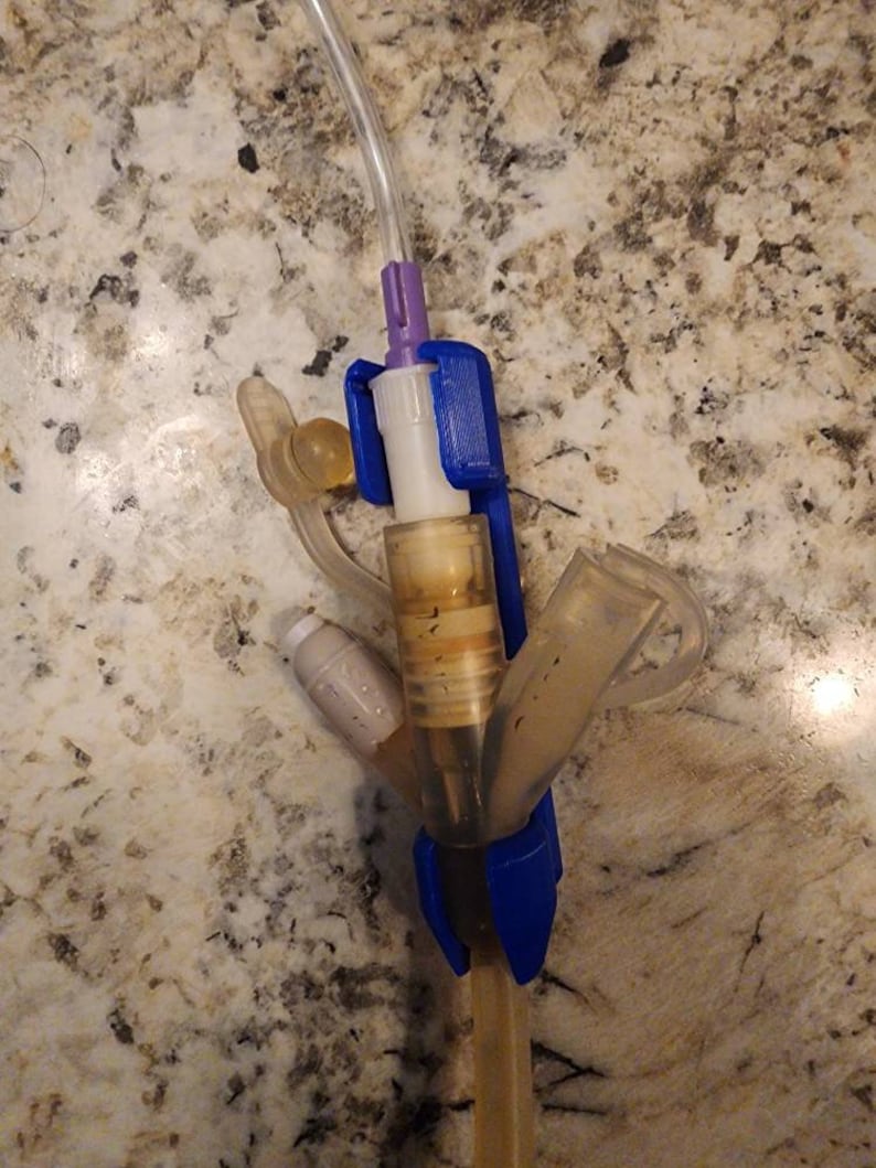 Puede incluir: Primer plano de un dispositivo m&eacute;dico con un conector de pl&aacute;stico azul y morado, un tubo transparente y un recipiente de pl&aacute;stico transparente. El dispositivo est&aacute; conectado a un tubo transparente.