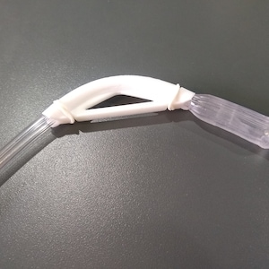 May include: A white plastic medical device with a clear plastic tube. The device has a handle with a curved shape and a clear plastic tip.