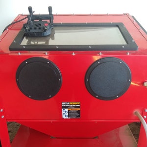 May include: Red sandblasting cabinet with two black round viewing ports, a clear glass window, and a black light fixture on top. The cabinet has a label that reads "Central Pneumatic".