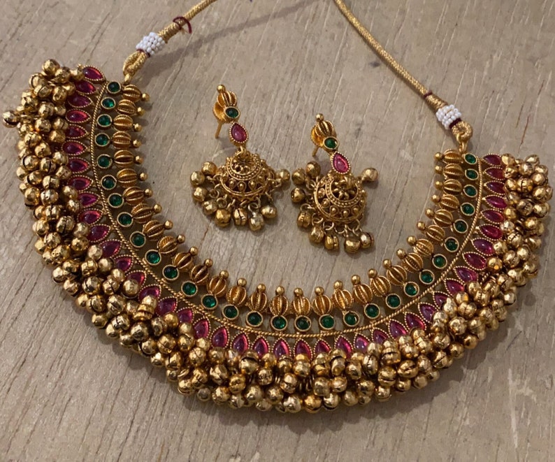 Op de afbeelding: Een gouden ketting met roze en groene stenen en een bijpassend paar oorbellen. De ketting heeft een rij kleine gouden balletjes langs de onderkant.