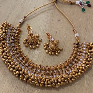 Op de afbeelding: Een gouden ketting en oorbellenset met witte parel accenten en een ontwerp van kleine ronde kralen. De ketting is een choker-stijl met een gebogen vorm.