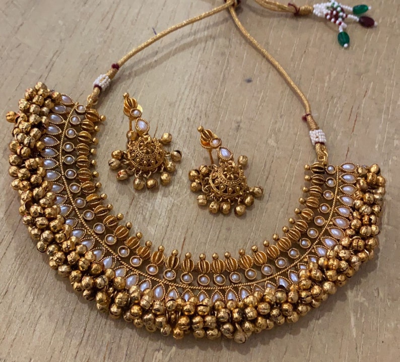 Op de afbeelding: Een gouden ketting en oorbellenset met witte parel accenten en een ontwerp van kleine ronde kralen. De ketting is een choker-stijl met een gebogen vorm.