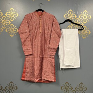 May include: A pink kurta with a white embroidered design and matching white trousers. The kurta has a mandarin collar and long sleeves.