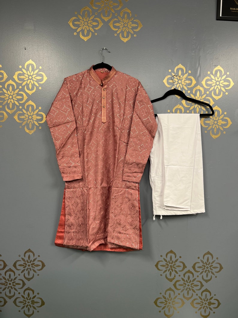 May include: A pink kurta with a white embroidered design and matching white trousers. The kurta has a mandarin collar and long sleeves.