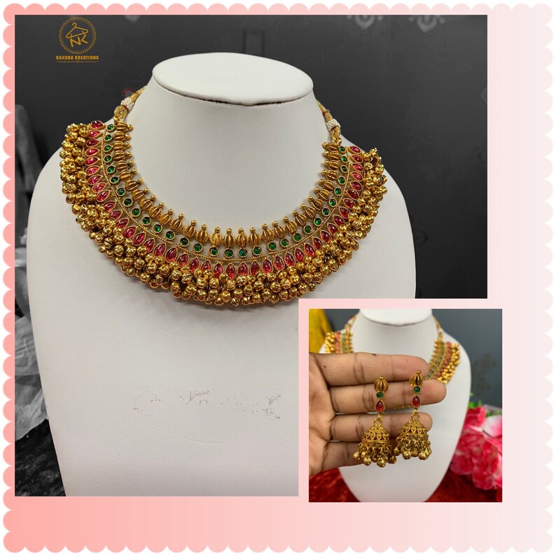 Op de afbeelding: Een gouden ketting- en oorsteensets met rode en groene stenen. De ketting heeft een gelaagd ontwerp met meerdere rijen gouden kralen en stenen. De oorbellen zijn van het hangende type met een klokvormig ontwerp.