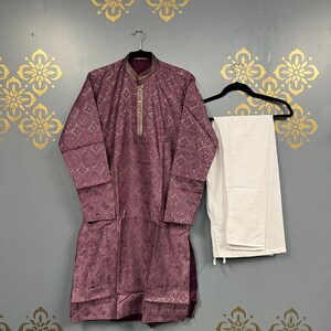May include: A purple kurta with gold embroidery and white trousers. The kurta has a button-up collar and a long-sleeved design.
