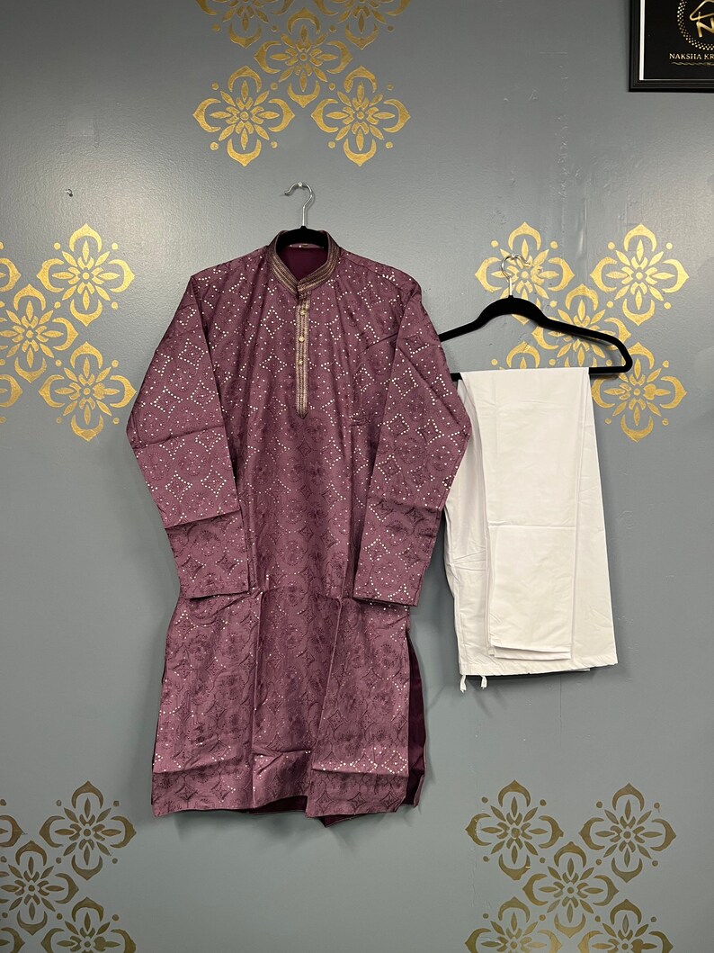 May include: A purple kurta with gold embroidery and white trousers. The kurta has a button-up collar and a long-sleeved design.