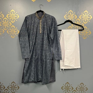 May include: A grey kurta with a white collar and silver embellishments, paired with white trousers. The kurta has a traditional Indian design and is hanging on a hanger.