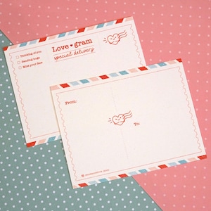May include: A blank postcard with a red heart and wings design. The postcard has a blue and pink striped border and says "Love gram special delivery" in red text. The postcard also has a checklist with the options "Thinking of you", "Sending hugs", and "Miss your face".