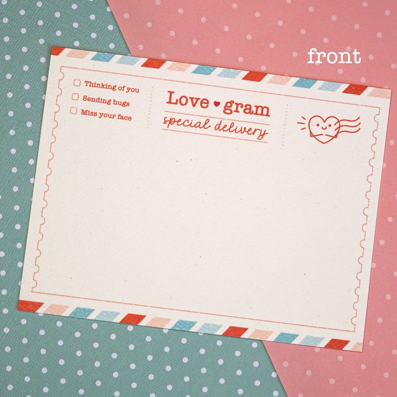 May include: A blank, cream-colored postcard with a red and blue border. The postcard has a red heart with a smiling face and the text "Love gram special delivery" on the top right corner. The text "Thinking of you", "Sending hugs", and "Miss your face" is written in a checklist format on the left side of the postcard.