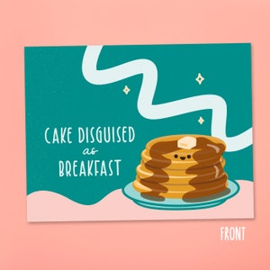 May include: A green card with a white wavy line and a stack of pancakes with a smiling face. The text on the card reads "Cake Disguised as Breakfast".