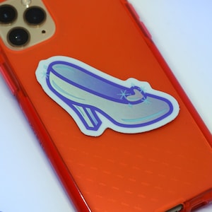 May include: A blue glass slipper sticker with a silver glitter design. The sticker is on a red phone case.