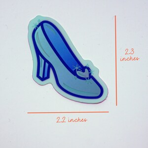 May include: A blue glass slipper sticker with a silver buckle and sparkles. The sticker is 2.2 inches wide and 2.3 inches tall.