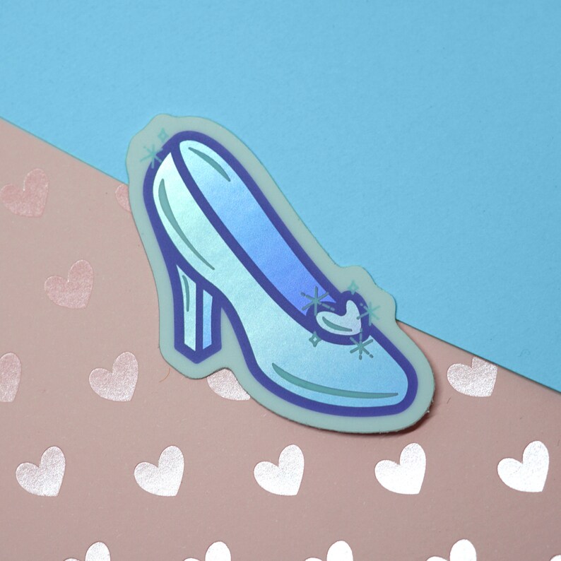 May include: A light blue glass slipper with a sparkly heart detail. The slipper is on a pink background with white hearts.