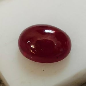 Może przedstawiać: Owalny, ciemnoczerwony kamień szlachetny o gładkiej, wypolerowanej powierzchni.