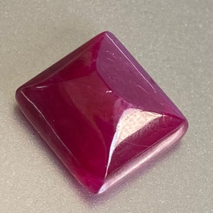 Op de afbeelding: Een dieprode edelsteen gesneden in een vierkante vorm met afgeschuinde randen. De edelsteen is gepolijst en heeft een glanzende afwerking.