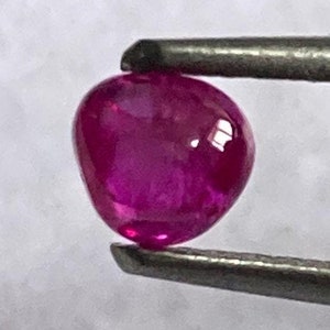 May include: A vibrant pink ruby gemstone, held by tweezers, with a smooth, polished surface.