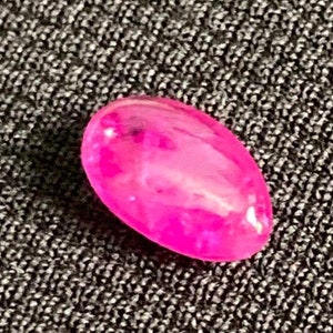 Könnte beinhalten: Ein leuchtend rosa ovaler Edelstein mit einem leichten Schimmer.