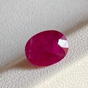 May include: A faceted, oval-shaped ruby gemstone. The ruby is a deep, rich red colour with a polished surface. The gemstone is set against a white background.
