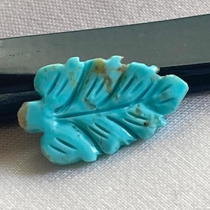 May include: A turquoise blue leaf-shaped cabochon gemstone with brown veins and a carved design.