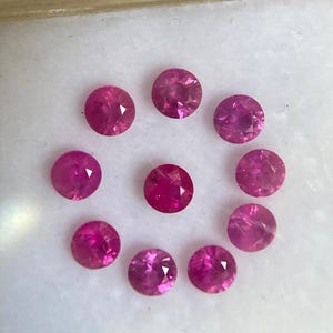 Peut inclure: Un ensemble de neuf pierres précieuses rondes, facettées et d'un rose éclatant, disposées en cercle. Chaque pierre présente une taille brillant avec de multiples facettes triangulaires qui reflètent la lumière, révélant une teinte magenta profonde.