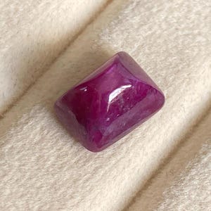 Op de afbeelding: Een diep paarse edelsteen met een vierkante vorm en een gepolijste afwerking.