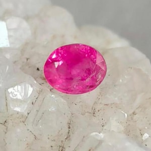 Könnte beinhalten: Ein leuchtend rosa ovaler Edelstein, wahrscheinlich ein Rubin, vor einem weißen Hintergrund.