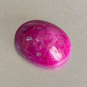 Op de afbeelding: Een levendige roze ovaalvormige edelsteen met een glad, gepolijst oppervlak. De steen heeft een lichte glans en een doorschijnende uitstraling.