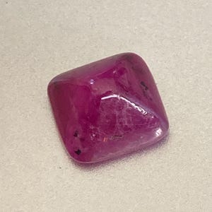 Op de afbeelding: Een vierkante, gefacetteerde, roze edelsteen met een lichte paarse tint. De edelsteen heeft een glanzende afwerking en is gezet in een bezel-setting.